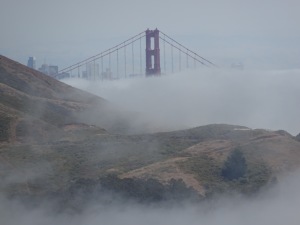 Fog-shrouded top of Golden Gate bridge, with Marin Headlands in foreground.